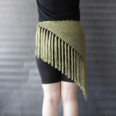 a woman wearing black shorts and a green crochet shawl is standing in front of a gray wall