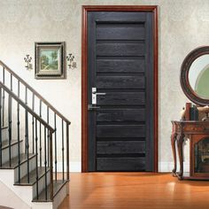 a black door is in front of a wooden stair case and mirror on the wall