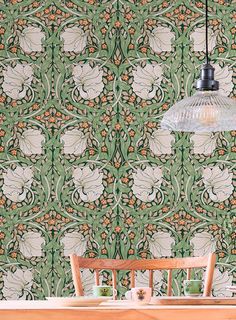 a wooden table sitting under a lamp next to a green wallpaper covered in flowers