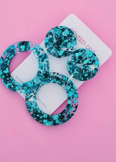 three pieces of blue and black glittered hair on a white card with pink background