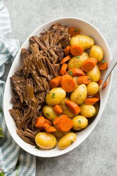 a bowl filled with meat, potatoes and carrots on top of a table next to a fork