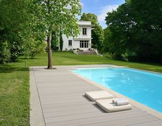 an empty swimming pool in front of a large white house with trees and grass around it