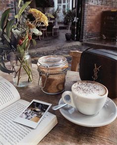 a cup of coffee sitting on top of a wooden table next to an open book