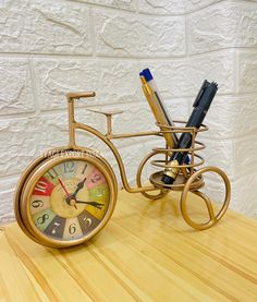 a golden bicycle clock sitting on top of a wooden table next to a pen holder