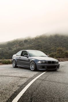 a grey car parked on the side of a road next to a hill covered in fog