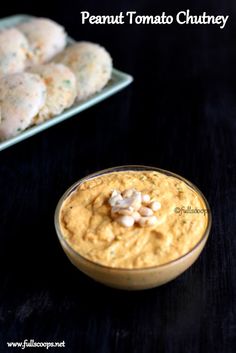 a bowl of hummus next to some crackers on a black table with text overlay that reads peanut tomato chutney