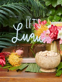 a table topped with lots of flowers next to a sign that says let's luau