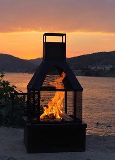 a fire pit sitting on top of a sandy beach next to the ocean at sunset