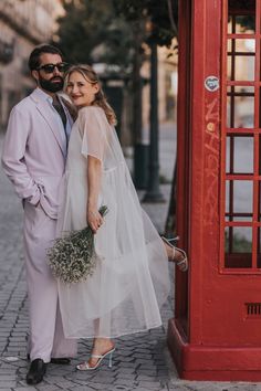 a bride and groom standing in front of a red phone booth on the side walk