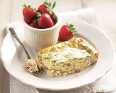 a white plate topped with a slice of quiche next to a bowl of strawberries