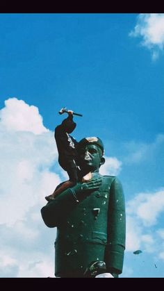 a statue of a man holding a baseball bat in front of a cloudy blue sky