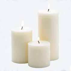 three white candles sitting next to each other on top of a snow covered ground,