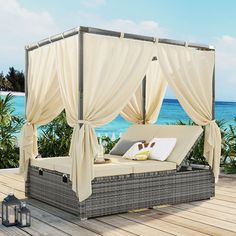 an outdoor daybed with curtains and pillows on the deck next to the ocean,