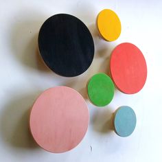 four different colored wooden discs on a white surface with one black, one pink, one green and one blue