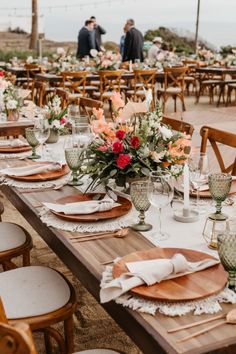 an outdoor table set up with place settings and flowers in vases on the tables