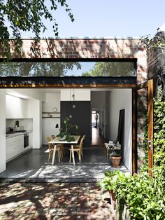 an open kitchen and dining room area with brick walls, white furniture and green plants