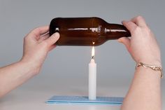 someone lighting a candle with a beer bottle in the shape of a candle on top of a table