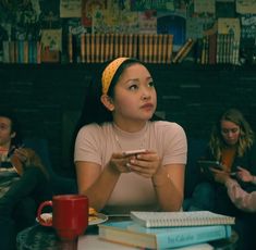 two women sitting at a table with books and a cup in front of them, looking up