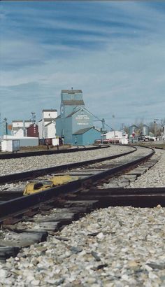 an old train track with some buildings in the back ground and rocks all around it