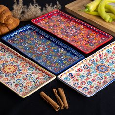 four colorful trays on a table with cinnamon sticks next to them and some bananas