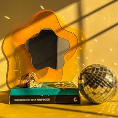 a mirror sitting on top of a yellow shelf next to a book and disco ball