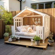 a dog laying on top of a white bed in a wooden decked area with potted plants