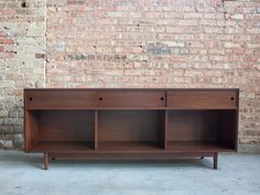 a wooden cabinet with three drawers in front of a brick wall