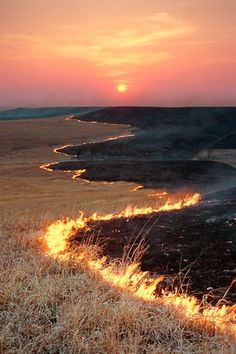 a fire hydrant on the side of a dry grass field at sunset with bright flames coming from it