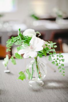 a vase filled with white flowers sitting on top of a table covered in greenery