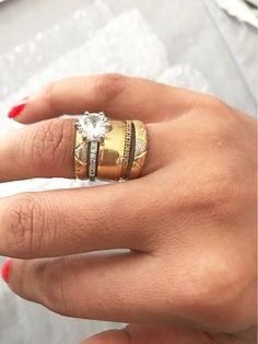 a woman's hand with two rings on top of her finger and an engagement ring in the middle