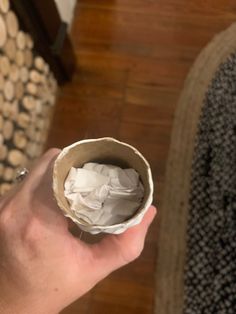 a hand holding a paper cup filled with toilet paper on top of a wooden floor