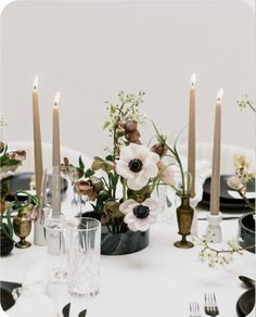 the table is set with candles and flowers in vases, plates, and silverware