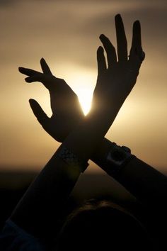 the sun is setting behind someones hands