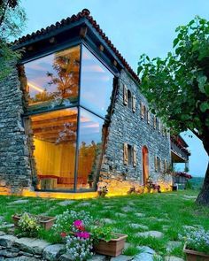 a house made out of stone and glass in the middle of a grassy area with trees