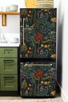 an old fashioned refrigerator is painted with flowers and plants on it's side, next to a green cabinet