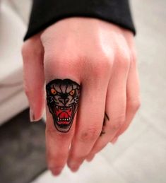 a person's hand with a black and red tiger tattoo on the middle finger