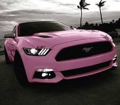 a pink mustang parked on the side of a road next to palm trees and clouds