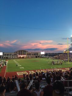 a stadium filled with lots of people watching a football game at sunset or dawn in the evening