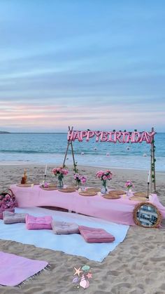 a birthday party setup on the beach with pink and purple decorations, flowers and candles