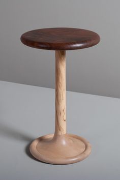 a small wooden table with a round top and wood base on a gray surface,