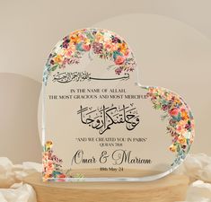 an islamic wedding card with floral design on the front and back, sitting on top of a wooden stand