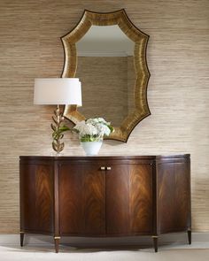 a large mirror on the wall above a wooden cabinet with a vase and flowers in it