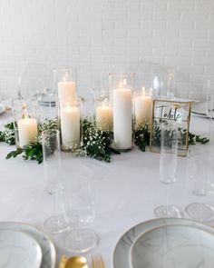 the table is set with white candles and greenery