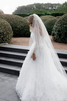 a woman in a wedding dress is walking down the steps with her veil over her face