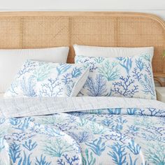 a bed with blue and white corals on it, next to a wicker headboard