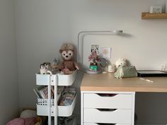 a white desk with a teddy bear on top and other items in the bottom drawer