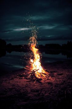 a bonfire is lit on the beach with dark clouds in the background and water behind it