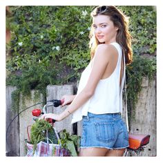 a woman standing next to a bike with a basket full of vegetables on the handlebars