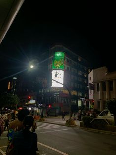 people are standing on the sidewalk in front of a tall building with a green sign