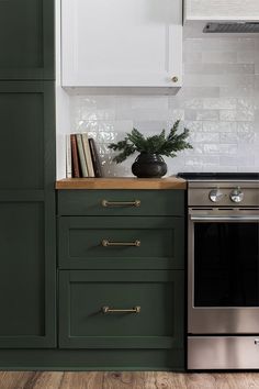 a kitchen with green cabinetry and white cupboards on the wall, along with a silver stove top oven